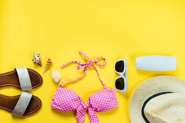 Top view of two pieces pink swimming suit and beach accessoties over yellow background. - Photo, Image
