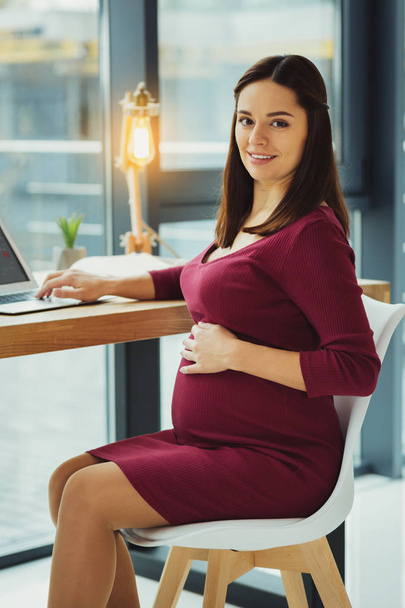 Belle secrétaire enceinte touchant son ventre et souriant
 - Photo, image