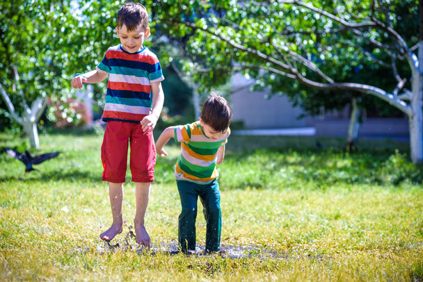 El niño y su hermano juegan en el parque de verano. Los niños con ropa colorida saltan en charco y barro en el jardín. Los niños caminan en el charco de verano después de la ducha. Diversión al aire libre por cualquier clima
. - Foto, imagen