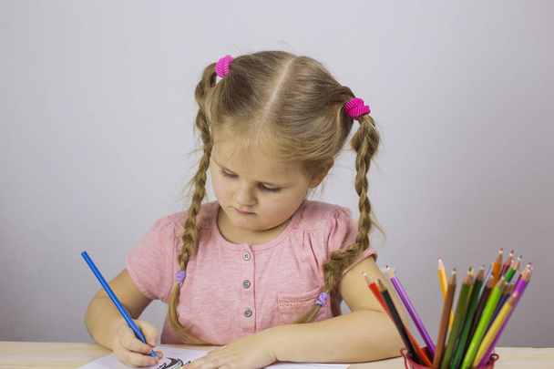 Young girl draws with colored pencils at a table - 写真・画像