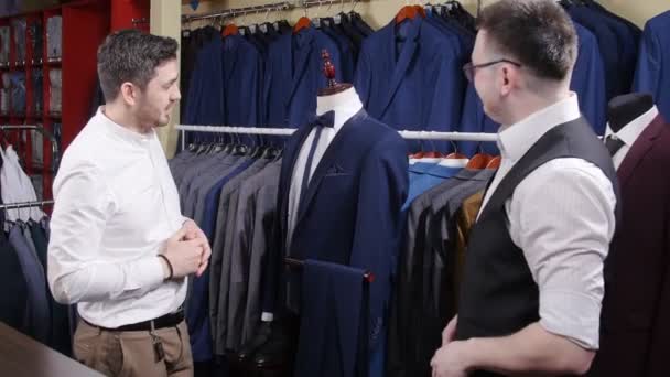 El hombre ayuda a otro a probar un traje en una tienda de ropa
 - Metraje, vídeo