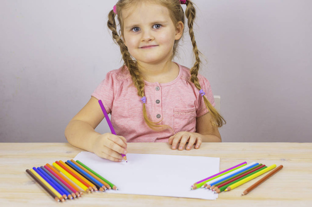 Preschool girl paints with colored pencils sitting at a table - 写真・画像