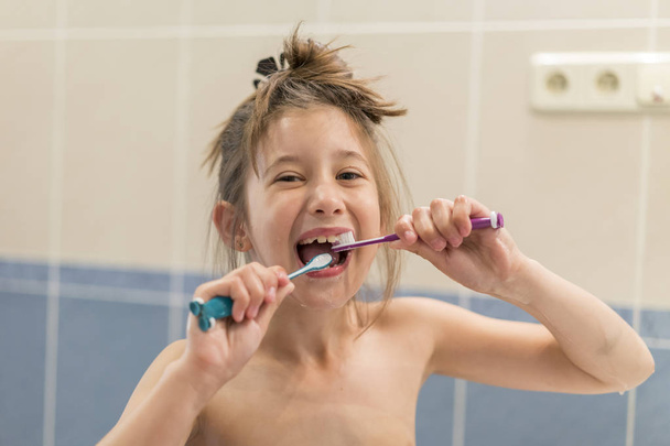 Menina escova os dentes com duas escovas. Estomatologia. cuidados de saúde oral
 - Foto, Imagem