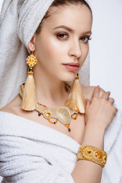 Young woman in a bathrobe and towel on her head, fashion golden jewelry, spa and care portrait, clean natural face, portrait on a background isolated - Foto, Bild