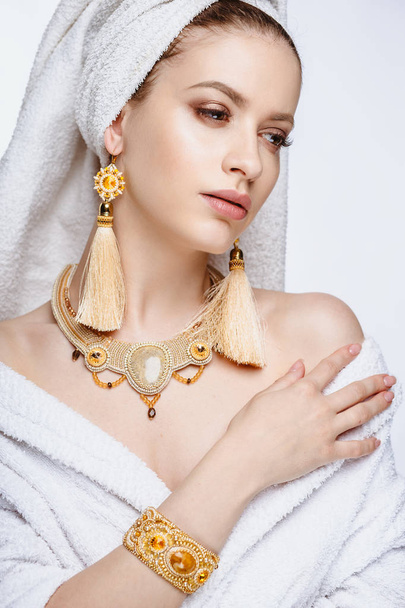 Mujer joven con albornoz y toalla en la cabeza, joyas de oro de moda, spa y retrato de cuidado, cara natural limpia, retrato sobre un fondo aislado
 - Foto, Imagen