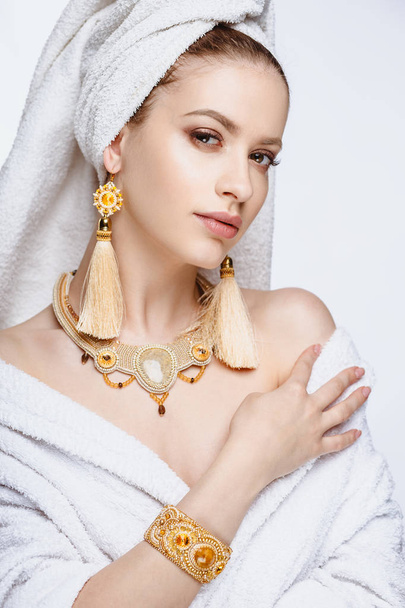 Young woman in a bathrobe and towel on her head, fashion golden jewelry, spa and care portrait, clean natural face, portrait on a background isolated - Fotó, kép