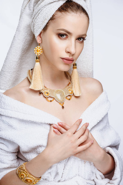 Young woman in a bathrobe and towel on her head, fashion golden jewelry, spa and care portrait, clean natural face, portrait on a background isolated - Foto, Imagem