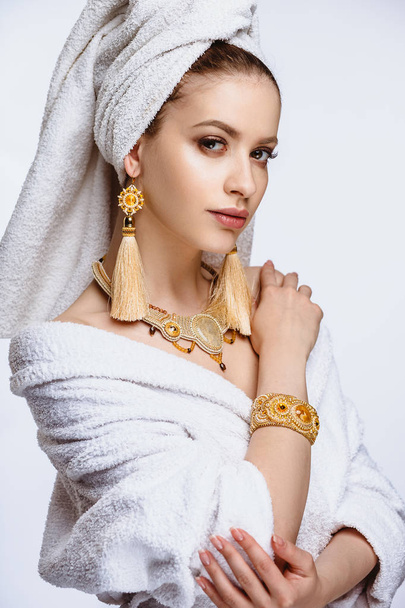 Young woman in a bathrobe and towel on her head, fashion golden jewelry, spa and care portrait, clean natural face, portrait on a background isolated - Foto, Imagen
