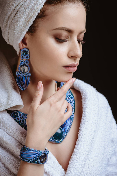 Young woman in a bathrobe and towel on her head, fashion jewelry, spa and care portrait, clean natural face, portrait on a dark background - Photo, Image