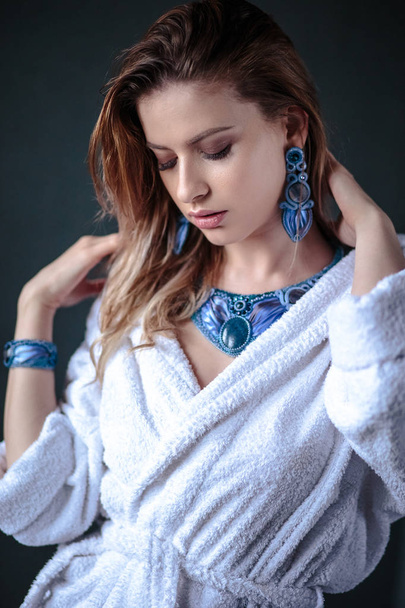 Young woman in a bathrobe and wet hair, fashion blue hand made jewelry, spa and care portrait, clean natural face, portrait on a background isolated - Zdjęcie, obraz