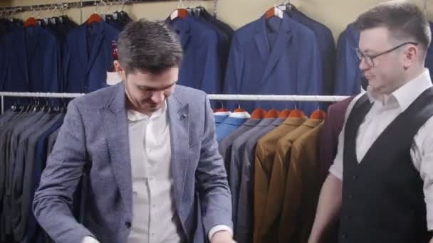 Άνδρας βοηθά μια άλλη δοκιμή για ένα κοστούμι σε ένα κατάστημα ιματισμού - Πλάνα, βίντεο