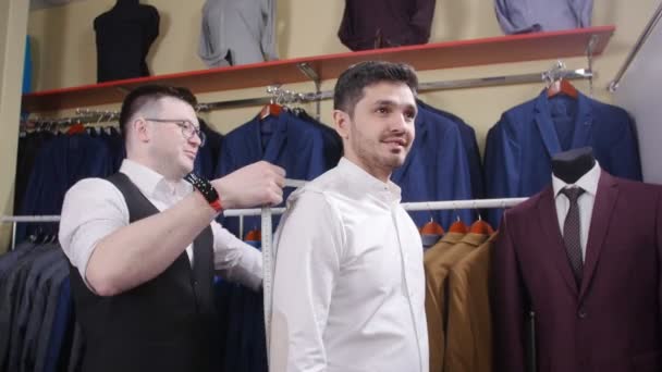 Mies auttaa toista kokeilemaan pukua vaatekaupassa
 - Materiaali, video