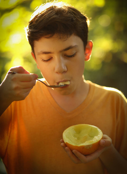 tiener jongen eten halve cut rijpe meloen met lepel - Foto, afbeelding