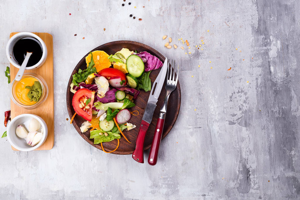 De plaat van de gezonde salade met tomaat, sinaasappel, walnoot, salade en komkommer, radijs met souce dressing op stenen achtergrond plat lag. Voeding en gezondheid. Schoon eten. - Foto, afbeelding