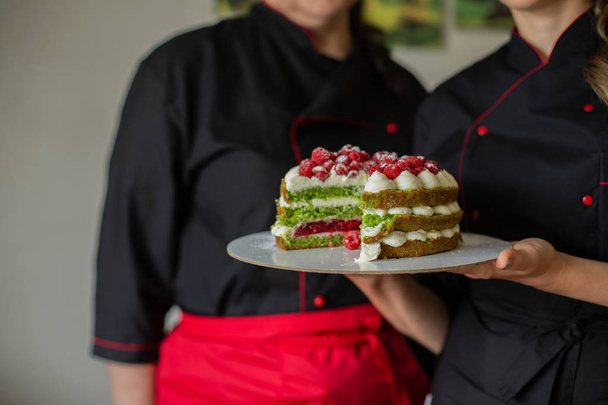 Konditorinnen in roten und schwarzen Arbeitsuniformen halten den Kuchen mit Beeren in der Küche. Konditor, Kuchen, Kochen.  - Foto, Bild