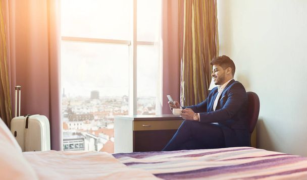 Smiling businessman using phone in hotel room - Photo, Image