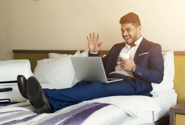 Επιχειρηματίας, μιλώντας σε φορητό υπολογιστή στο δωμάτιο του ξενοδοχείου - Φωτογραφία, εικόνα