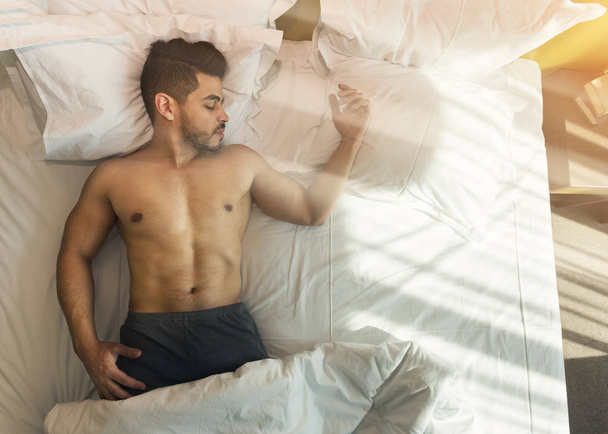 Bovenaanzicht van shirtless jonge man slapen in bed - Foto, afbeelding