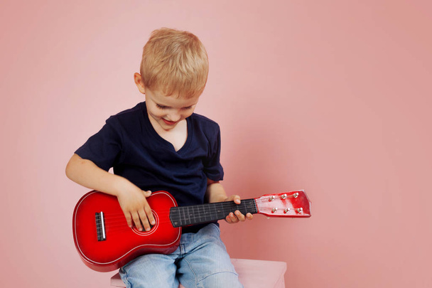 Little boy is learning to play on a small guitar. Study music. Ukulele - Zdjęcie, obraz