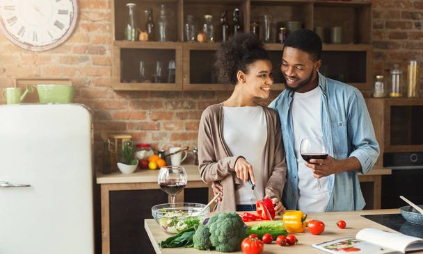 liebevolles afrikanisch-amerikanisches Paar bereitet Salat zu und trinkt Rotwein - Foto, Bild