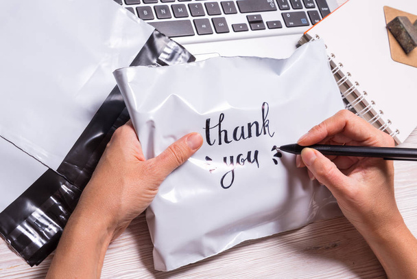Woman hands writing Thank you text on polyethylene envelope  - Foto, afbeelding