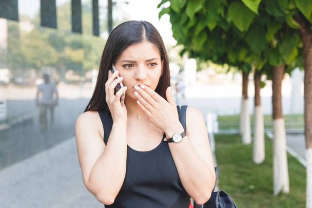 Portrait of a shocked young girl speaking on the phone in park - Φωτογραφία, εικόνα