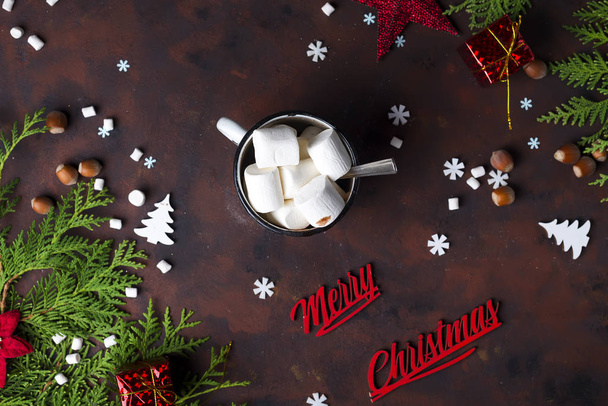 Ветки елки с рождественскими игрушками, подарочные коробки, чашка горячего зефира какао и снежинки на бетонном коричневом фоне, с текстом Счастливого Рождества
 - Фото, изображение