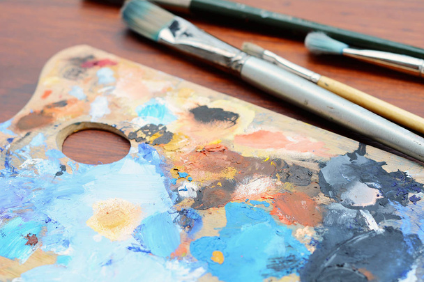 Artist's palette with colorful oil paint strokes and paintbrushes on wooden background. Art concept - Foto, Imagen