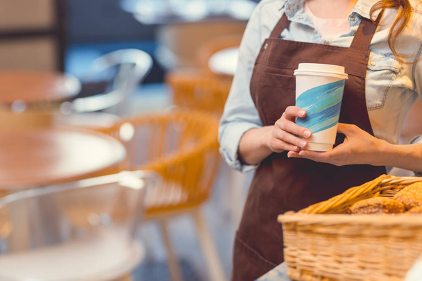 Mujer joven en uniforme con una taza de café en la panadería
 - Foto, imagen