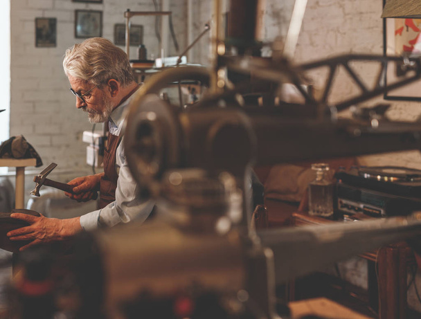 Un zapatero anciano en un delantal en un taller
 - Foto, Imagen