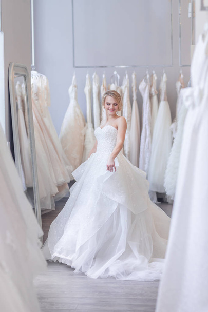 Smiling girl in a white dress in wedding shop - Фото, изображение