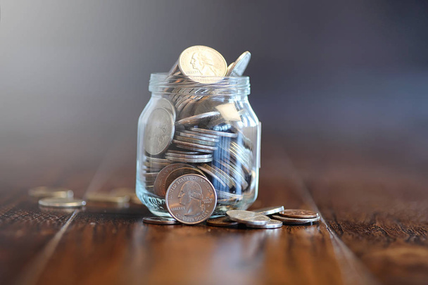 Coins in a glass jar on a wooden floor. Pocket savings from coin - Photo, image