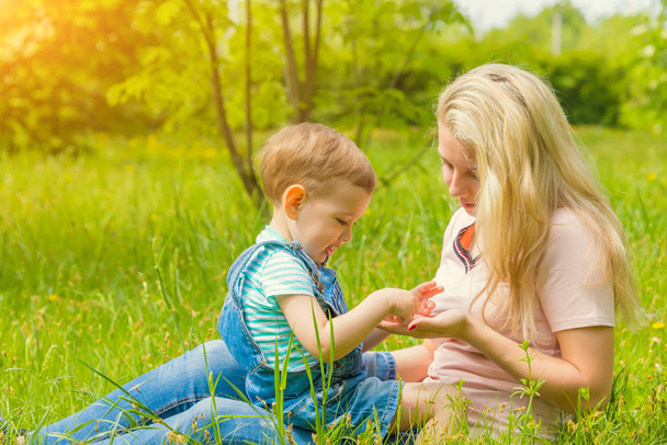 mother and child in nature in the Park, resting on the green grass in Sunny weather, happy family - Fotografie, Obrázek