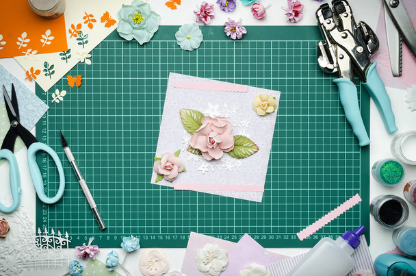 Multi-colored paper crafts on the cutting mat and scrapbooking tools, top view - Photo, Image