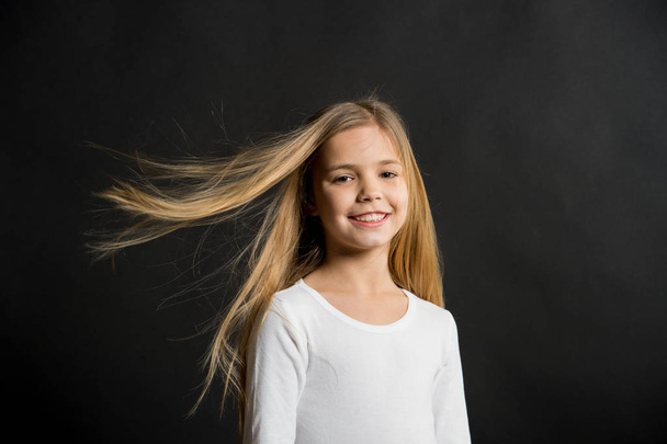 Little girl smile with long blond hair on black background. Happy child with fashion hairstyle. Beauty kid smiling with adorable look. Beauty salon. In this salon we love hair - Foto, afbeelding