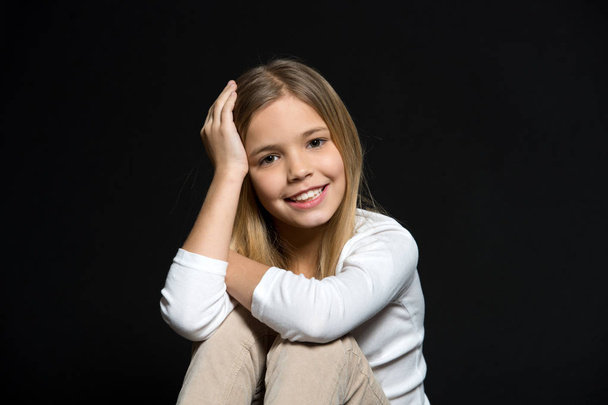 Beauty kid smiling with adorable look on black background. Beauty salon. The salon that leaves a smile on your face. Little girl smile with long blond hair. Happy child with fashion hairstyle - Фото, зображення