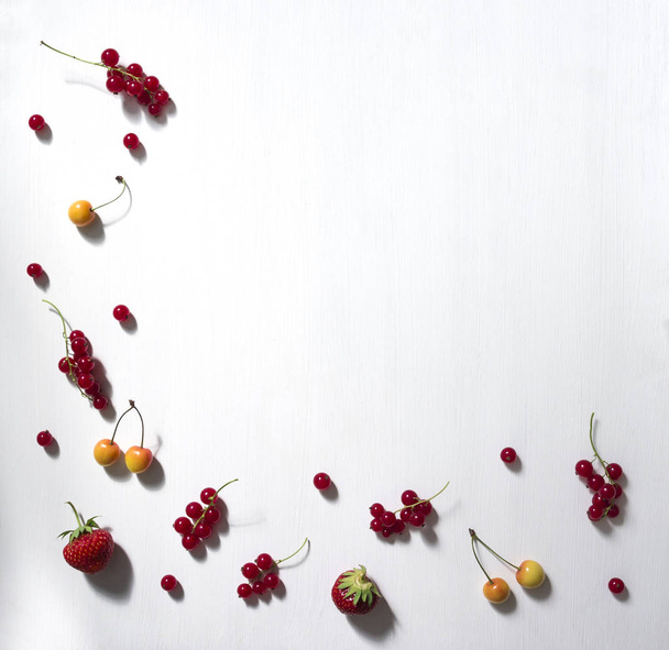 on a white background frame with the edge and from below lie berries and twigs currant red strawberry cherry white pattern copy space - 写真・画像