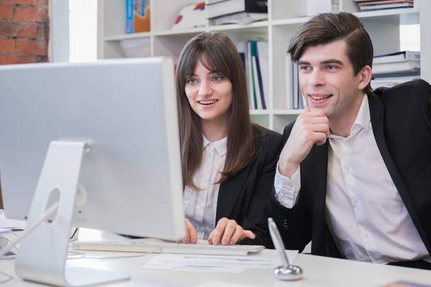 Liikemiehet työskentelevät toimistossa, etsivät yhdessä tietokoneen monitoria ja hymyilevät
 - Valokuva, kuva