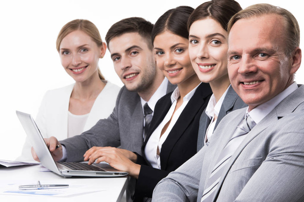 Ryhmä luottavaisia hymyileviä liikemiehiä istumassa yhdessä peräkkäin kannettavalla tietokoneella, eristettynä valkoisella taustalla
 - Valokuva, kuva