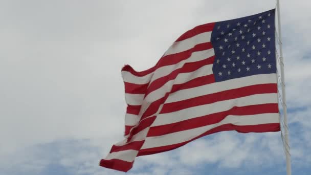 breite, stetige Aufnahme einer Flagge der Vereinigten Staaten, die im Wind weht, mit blauem und weißem Himmel im Hintergrund - Filmmaterial, Video