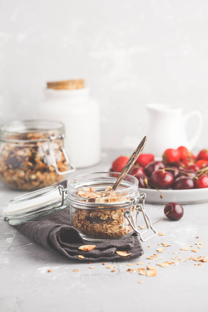 Homemade oat granola in glass jars with cherry and yogurt. Healthy food concept. - Photo, Image