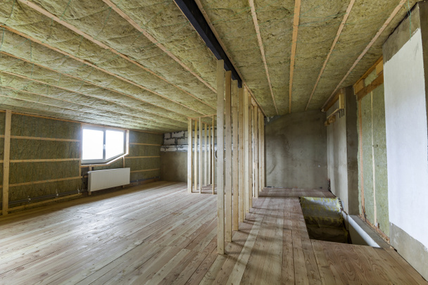 Construction and renovation of big light spacious empty room with oak floor, walls and ceiling insulated with rock wool, heating radiators under low attic windows and wooden frame for future walls. - Photo, Image