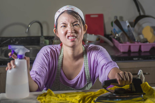 young pretty frustrated and stressed Asian Chinese woman with iron working at home kitchen ironing clothes desperate and overwhelmed in house maid service housework domestic stress - Φωτογραφία, εικόνα