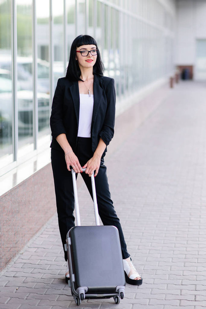 Молодая красивая девушка в деловом костюме и в солнечных очках с чемоданом
. - Фото, изображение