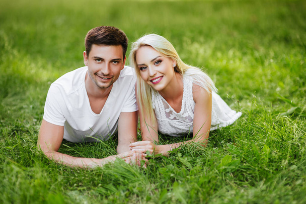 The lovely beautiful couple in love sitting on green grass. Romantic love story in the park. Young girl and boy in love. - Valokuva, kuva
