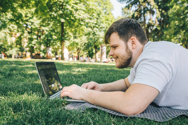молодий дорослий чоловік працює на ноутбуці в міському парку в літній день
 - Фото, зображення