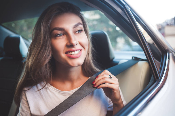 Piękna kobieta z telefonem uśmiechnięta siedząc na tylnym siedzeniu w samochodzie. - Zdjęcie, obraz