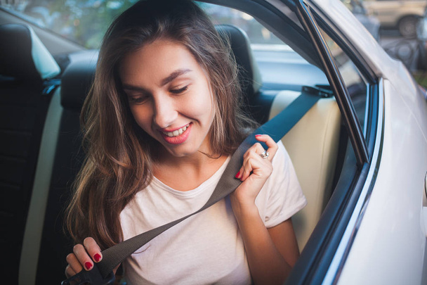 Piękna kobieta z telefonem uśmiechnięta siedząc na tylnym siedzeniu w samochodzie. - Zdjęcie, obraz