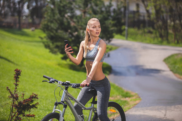 Calm woman is using phone while cycling - Zdjęcie, obraz