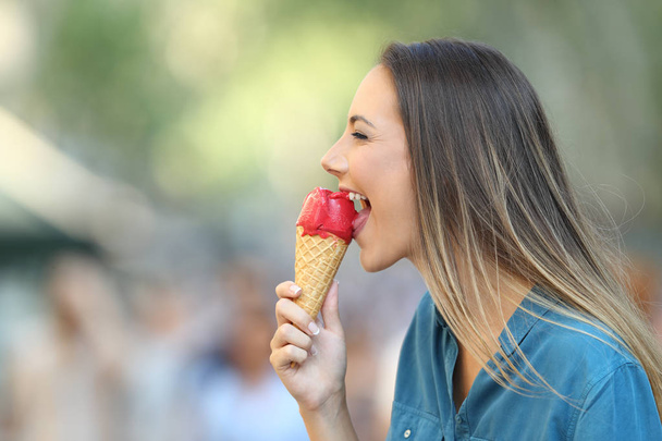 Side view portrait of a happy woman biting an ice cream on the street - 写真・画像
